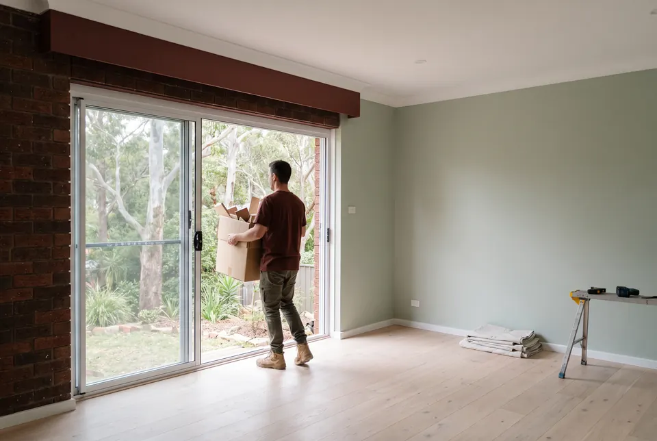 A renovated living room just after handover, a crew member carrying the last box of offcuts out through the sliding door