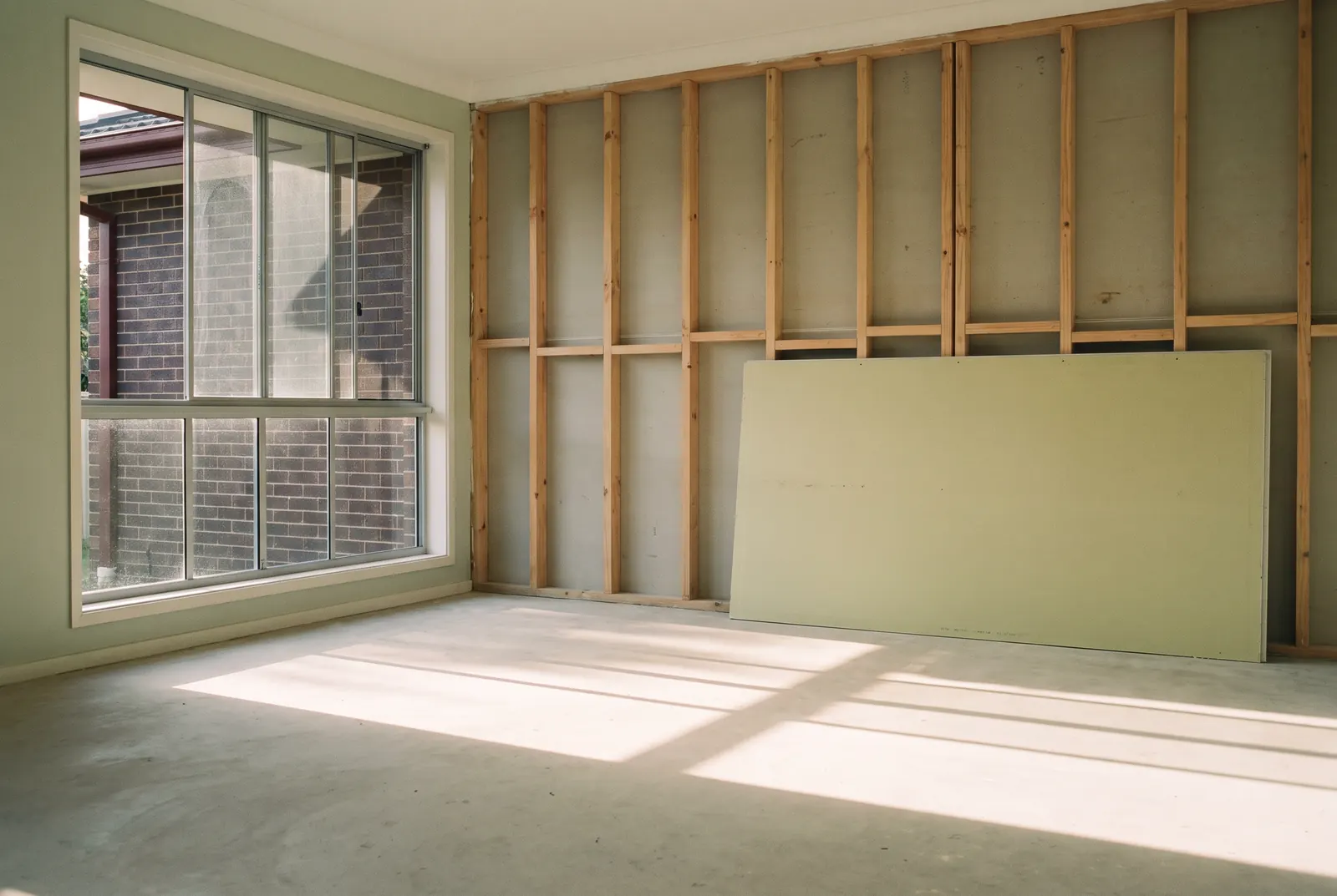 An emptied room, the floor swept, the back wall stripped to new pine framing and the first sheet of wet-area board leaning against it