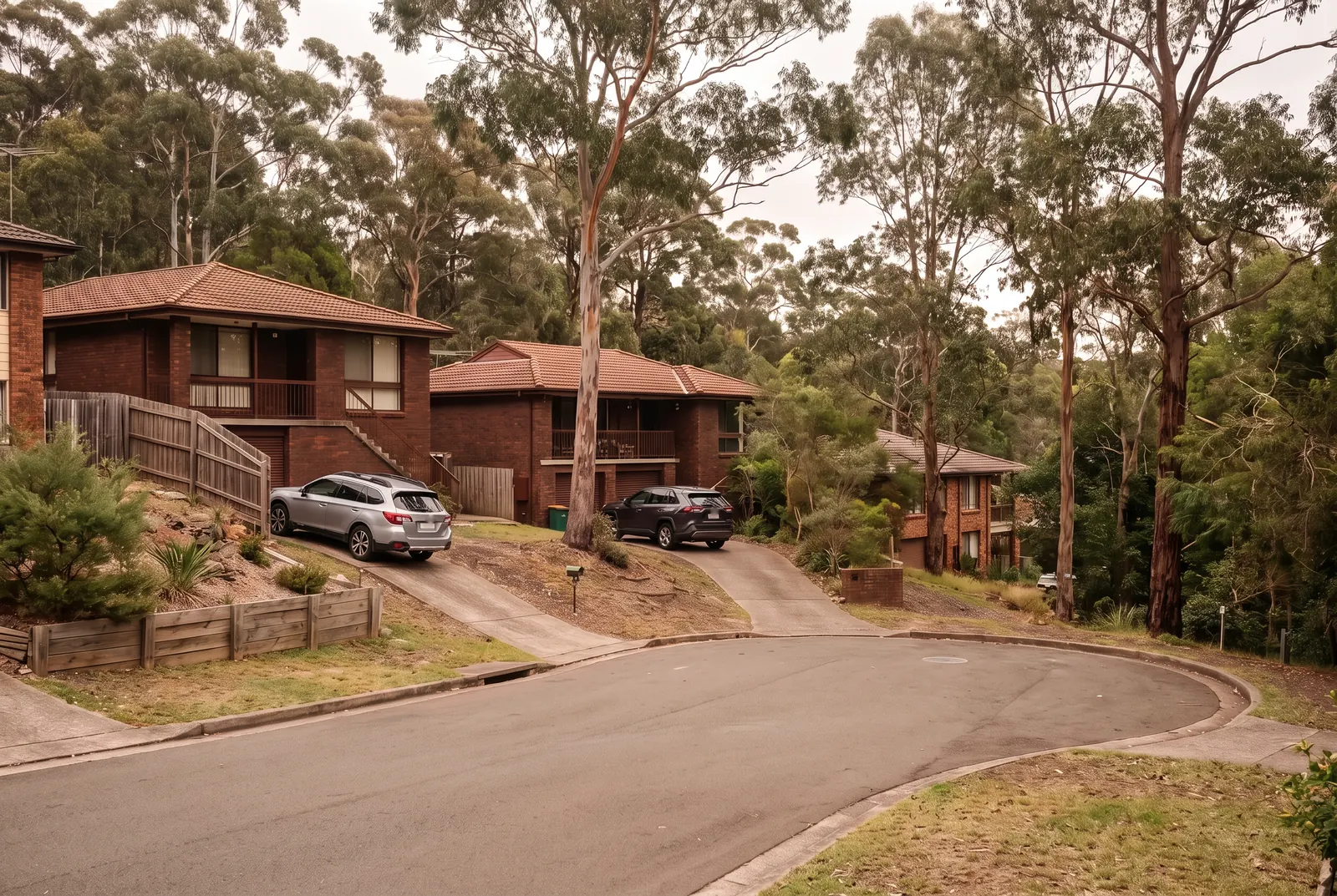 A quiet curving street of split-level brick houses on sloping blocks, bushland behind, ending in a turning circle